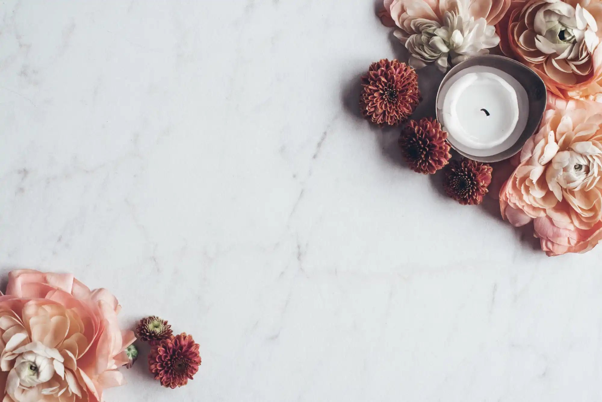 White candle surrounded by pink and burgundy flowers on a marble surface.